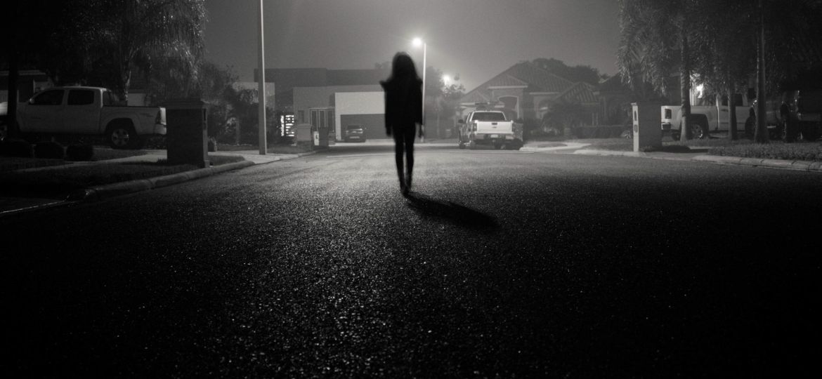 Girl walking in an urban Street at night under streetlights